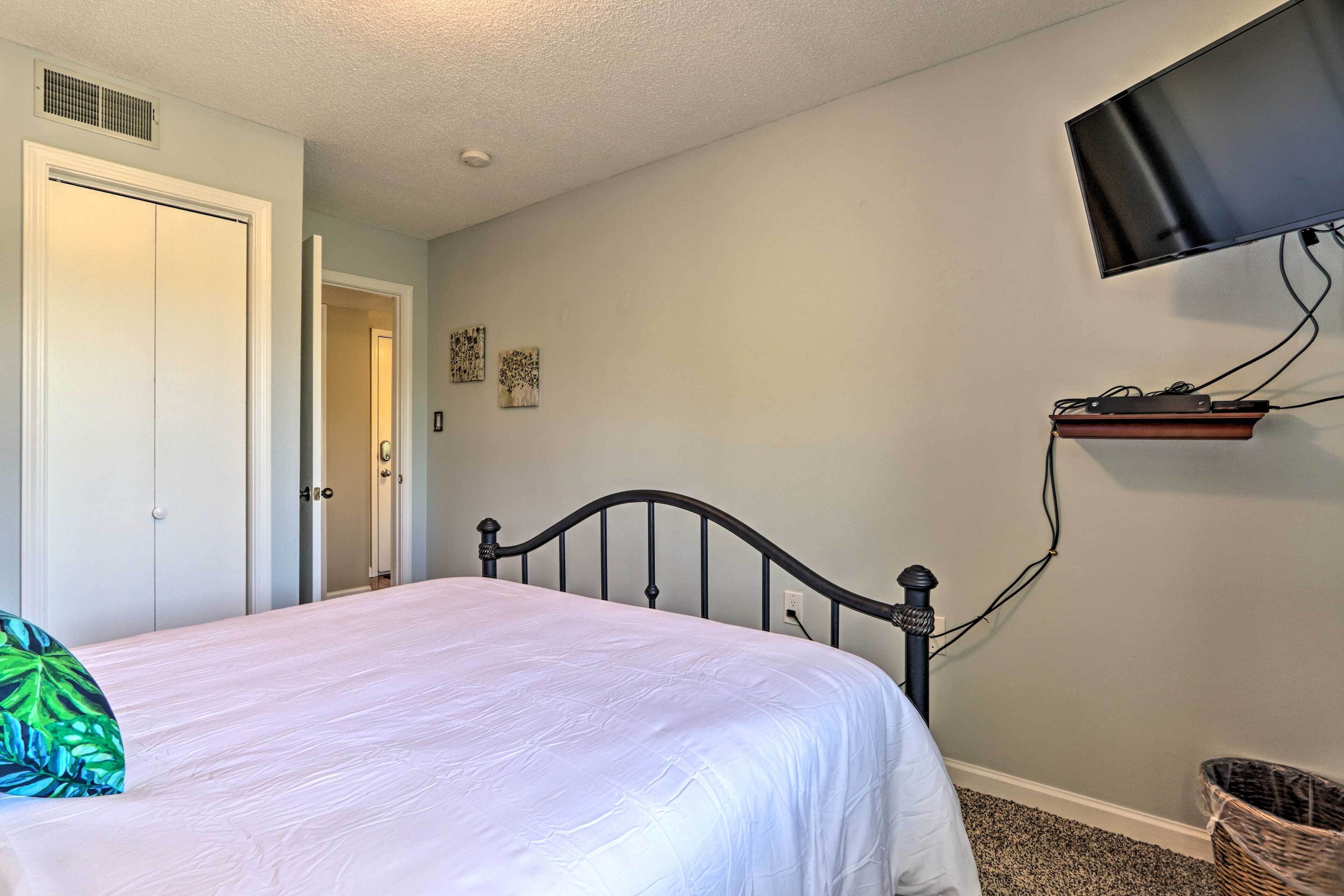 A bedroom with a bed, a television mounted on the wall, and a door leading to another room.