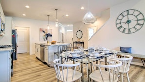 A modern kitchen with white cabinetry, a dining area with a glass table, and a large wall clock.