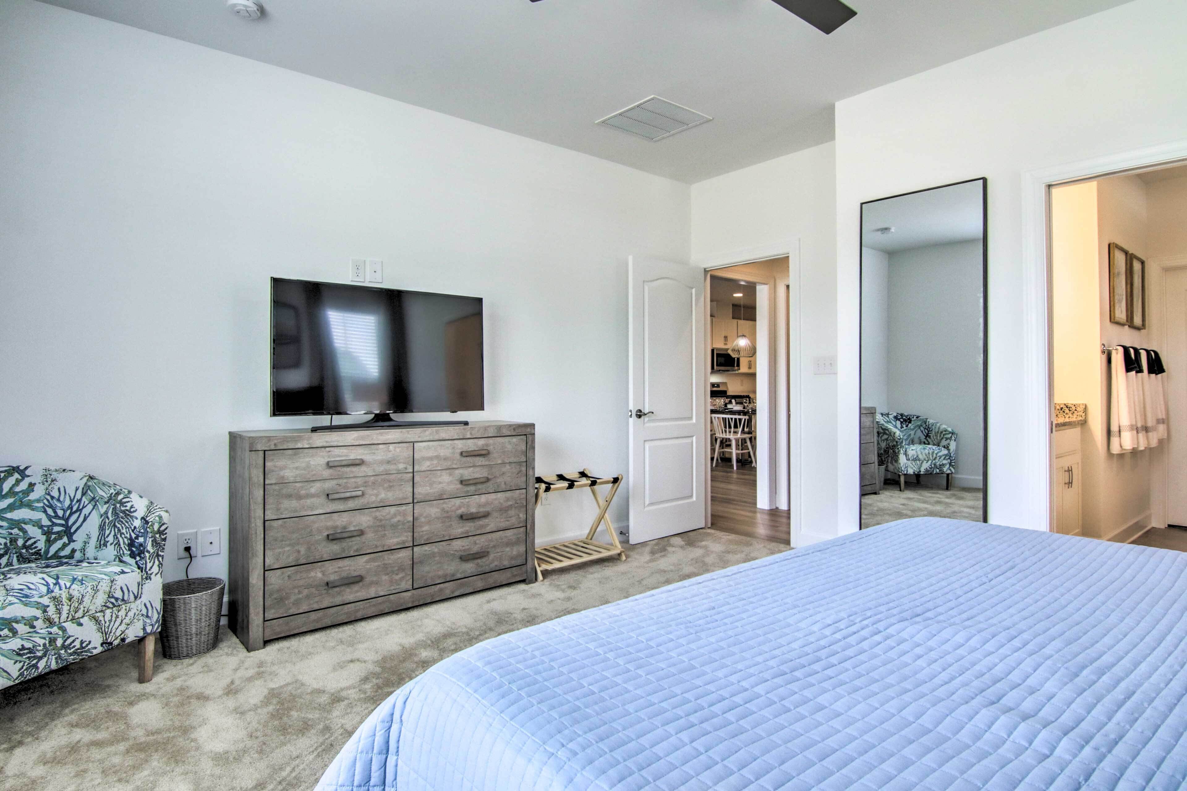 A bedroom with a large bed, a TV on a dresser, a walk-in closet, and a door leading to another room.