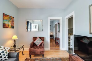 A living room with a brown leather armchair, a glass coffee table, a lamp, and a colorful painting on the wall. - 'St Ceilia' Apt - Walk to Bisbee Attractions! (Bisbee)