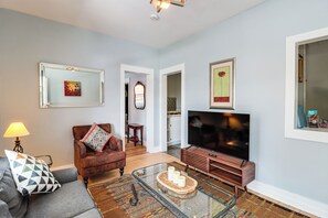A living room with a sofa, armchair, coffee table, TV, and artwork on the walls. - 'St Ceilia' Apt - Walk to Bisbee Attractions! (Bisbee)