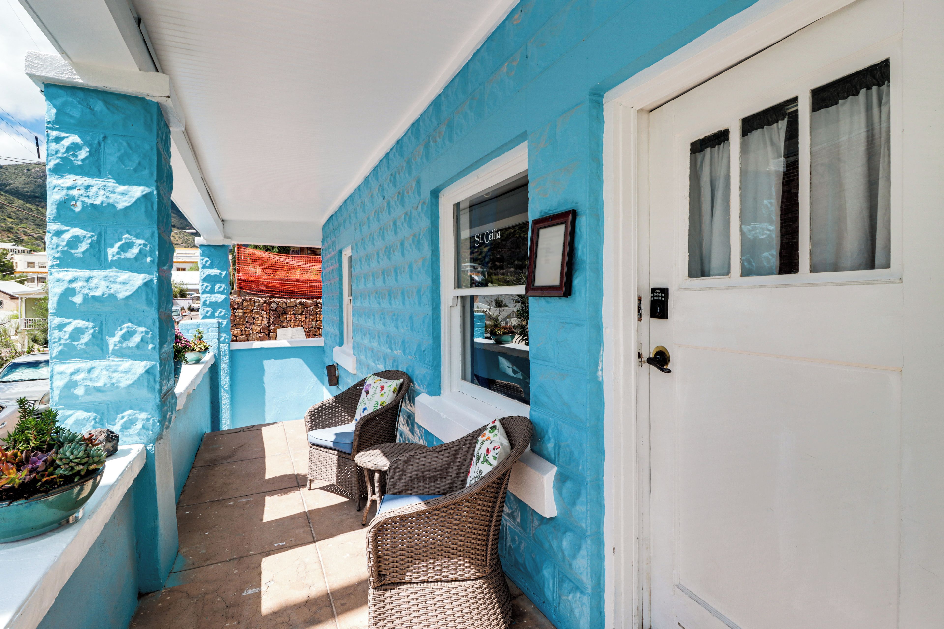 Un espace extérieur aménagé, abrité et doté de meubles en osier et d’un mur bleu.