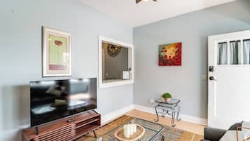 A living room with a flat-screen TV, a framed artwork, a decorative mirror, and a door with curtains.