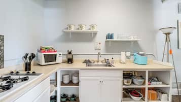 Een kleine keuken met een magnetron, spoelbak en verschillende opbergkasten.