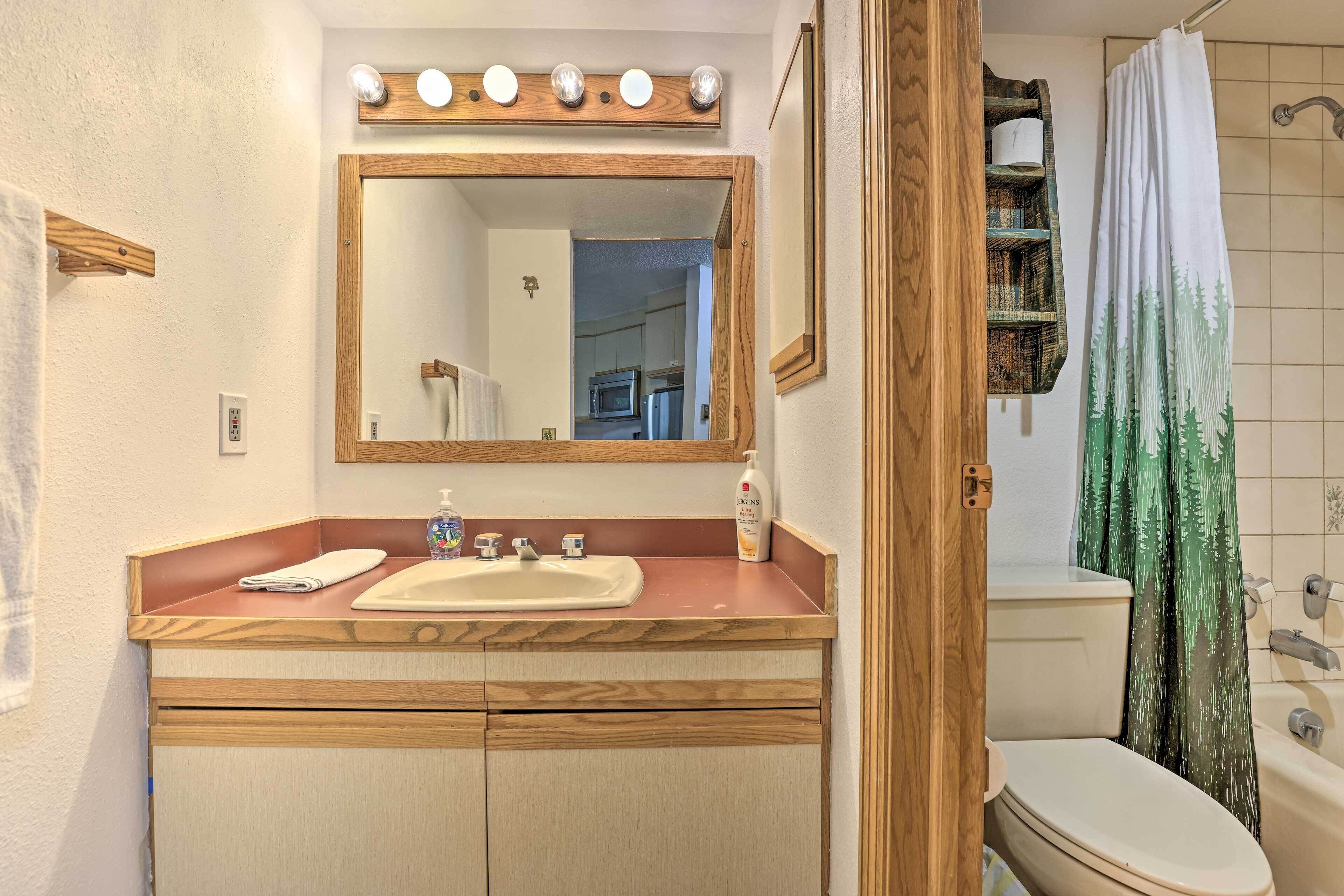 A bathroom with a wooden vanity, a mirror with lights, a sink, a toilet, and a shower curtain.