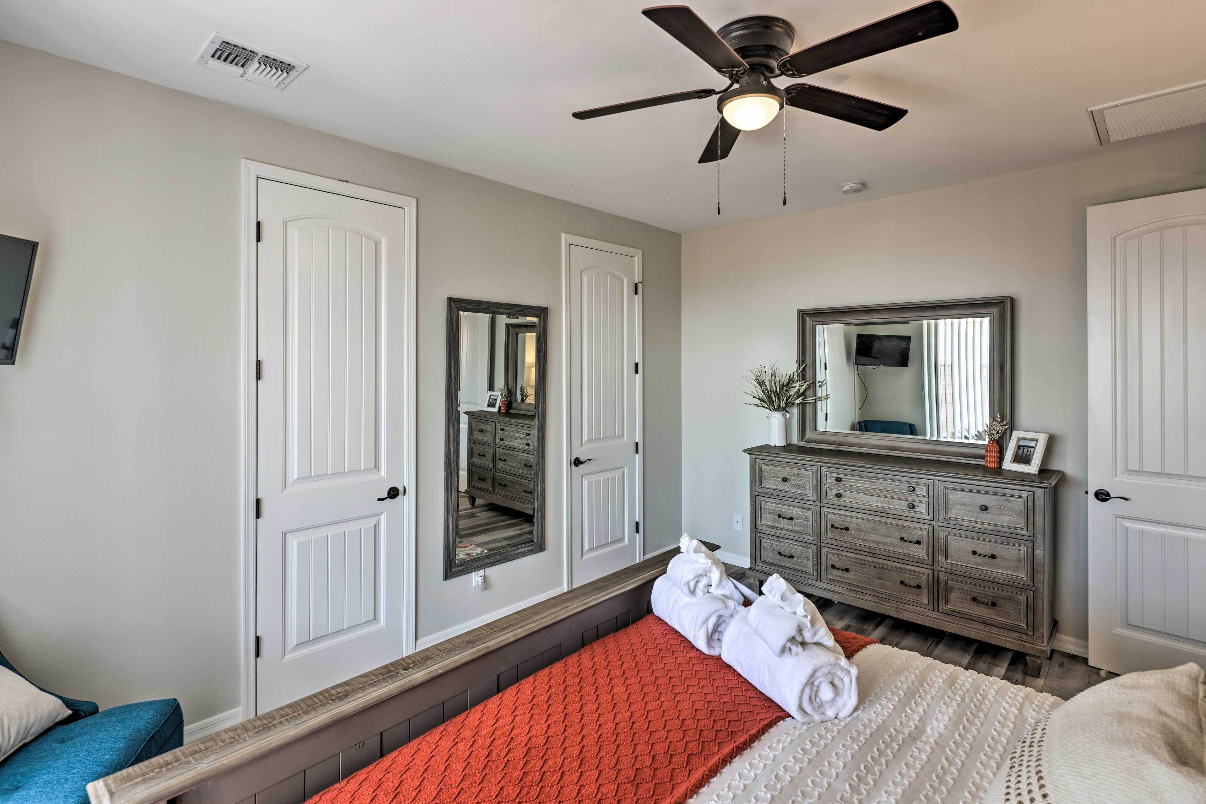 A bedroom with a bed, a dresser, a mirror, and a ceiling fan.