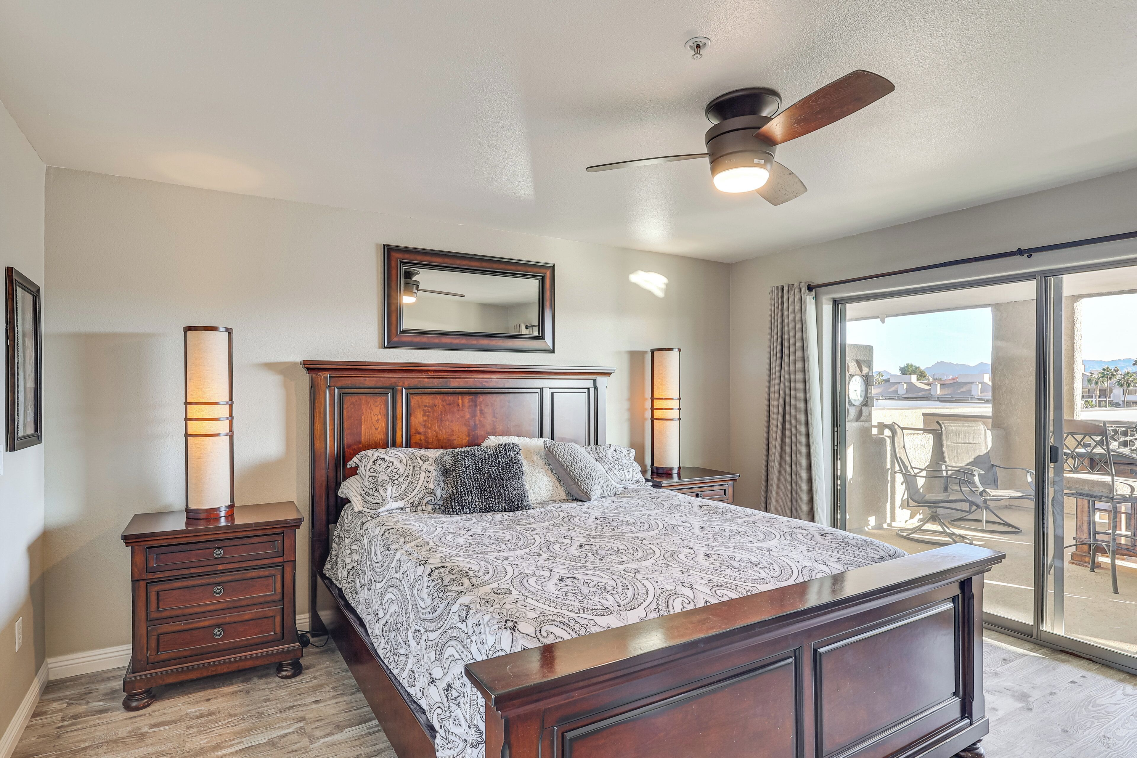 A bedroom with a large bed, wooden headboard, a ceiling fan, and a view through a sliding glass door.