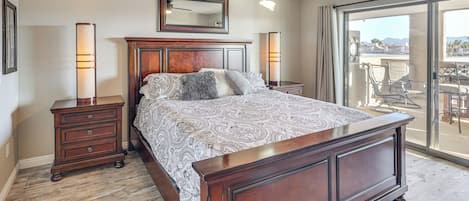 A bedroom with a large bed, wooden headboard, a ceiling fan, and a view through a sliding glass door.