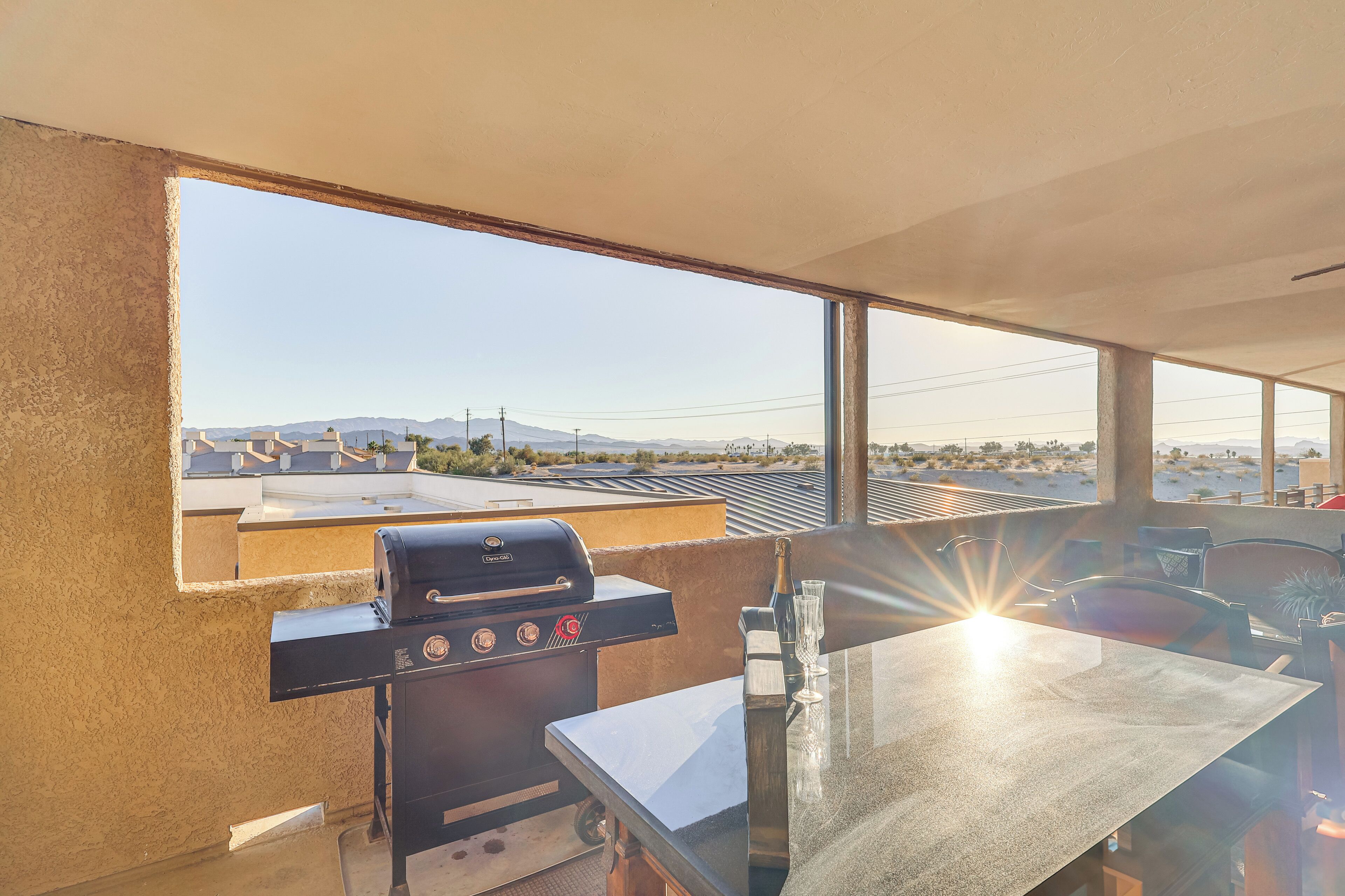 A balcony with a grill, a table, and a view of a cityscape.