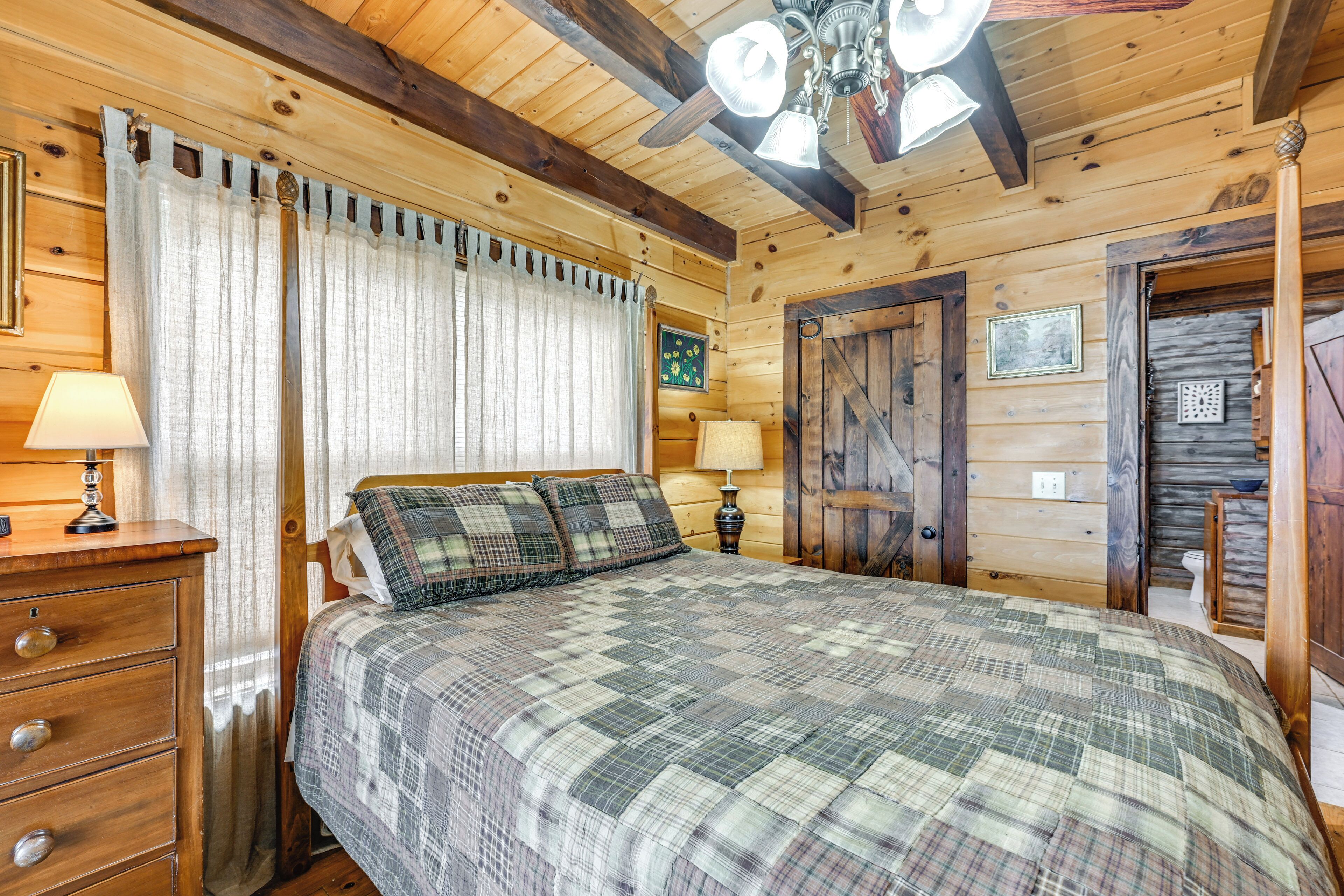Une chambre à coucher dans une cabane en bois, avec un lit, deux lampes de chevet, une commode et un ventilateur de plafond.