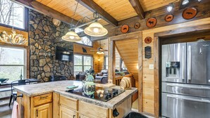 Une cuisine avec des meubles en bois, un mur en pierre, un grand îlot central, des appareils électroménagers en acier inoxydable et un luminaire suspendu.