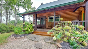 Un chalet rustique en rondins de bois, doté d’un porche, d’un chemin de pierre et d’un jardin luxuriant.