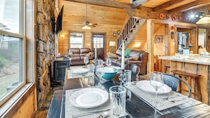 Un intérieur en bois avec une table à manger pour quatre personnes, une cheminée et un escalier menant à un niveau supérieur.