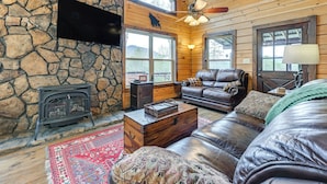 Un intérieur de chalet chaleureux avec un mur en pierre, un plafond en bois, des meubles en cuir, une cheminée et de grandes fenêtres.