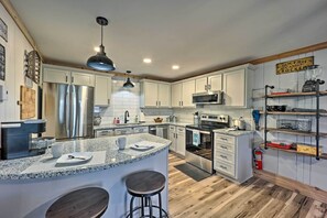 A modern kitchen with white cabinets, stainless steel appliances, a granite countertop, and a bar area with stools. - 1 Mi to Skiing: Beech Mountain Condo w/ Fireplace! (Banner Elk)
