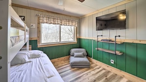 A bedroom with a bunk bed, a small sofa, a ceiling fan, a window with a view, and a mounted TV. - 1 Mi to Skiing: Beech Mountain Condo w/ Fireplace! (Banner Elk)