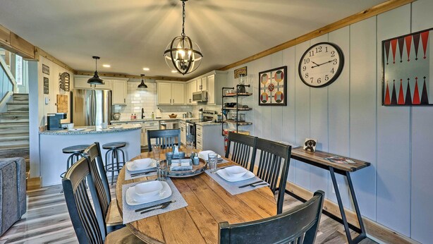 A modern kitchen with white cabinets, a wooden dining table set for four, and a large clock on the wall. - 1 Mi to Skiing: Beech Mountain Condo w/ Fireplace! (Banner Elk)