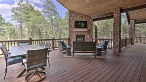 A covered outdoor deck with stone walls, a stone fireplace, and a television. - Stylish Show Low House w/ Expansive Deck! (Show Low)