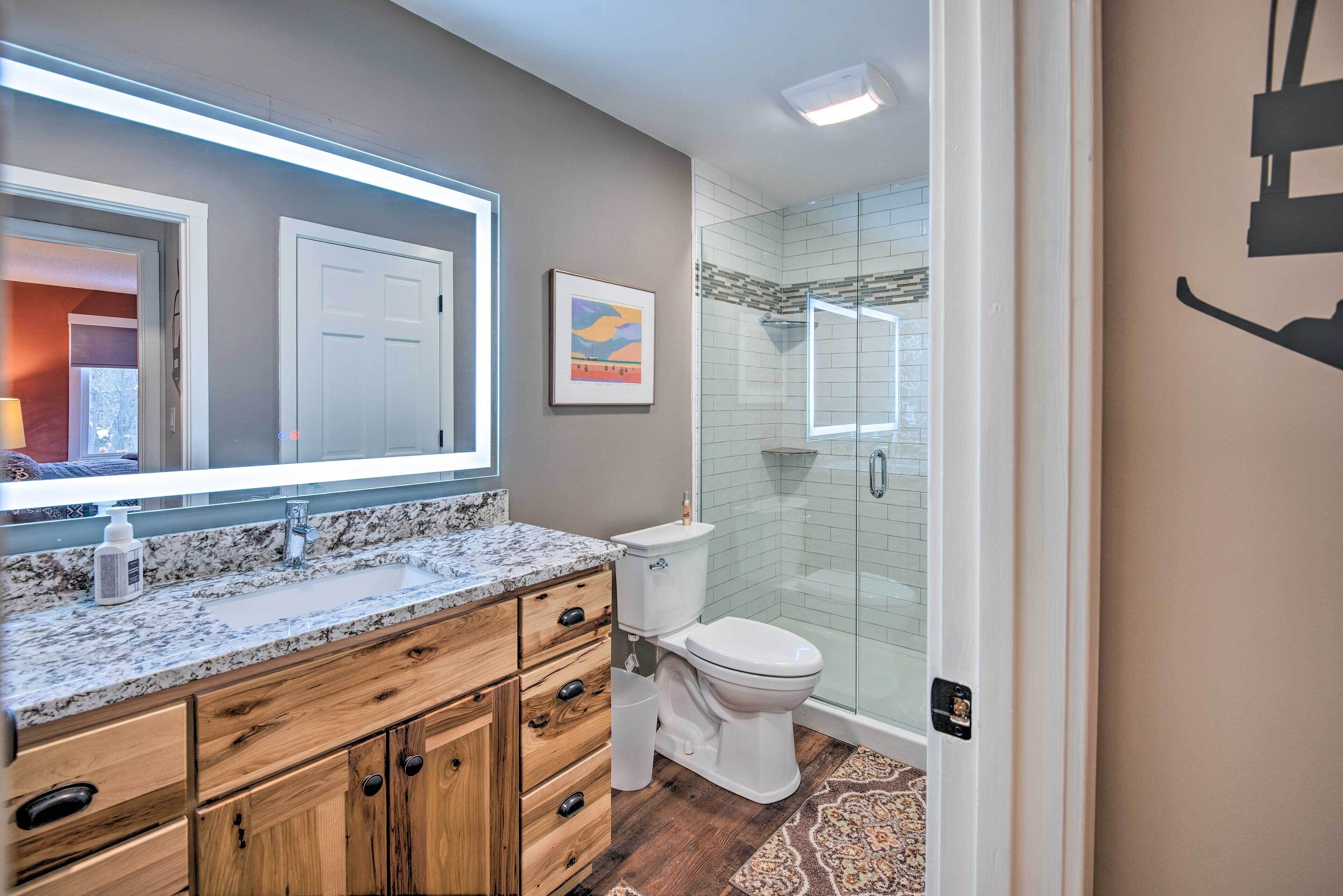 A modern bathroom with a granite countertop, wooden cabinets, a white toilet, and a glass shower enclosure.