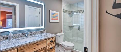 A modern bathroom with a granite countertop, wooden cabinets, a white toilet, and a glass shower enclosure.