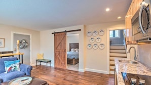 A modern living room with a sofa, ottoman, and a coffee table. There is a sliding barn door leading to a bedroom. The kitchen has a granite countertop and stainless steel appliances. - Spacious Village of Loon Home < 1 Mi to Ski Slopes (Lincoln)