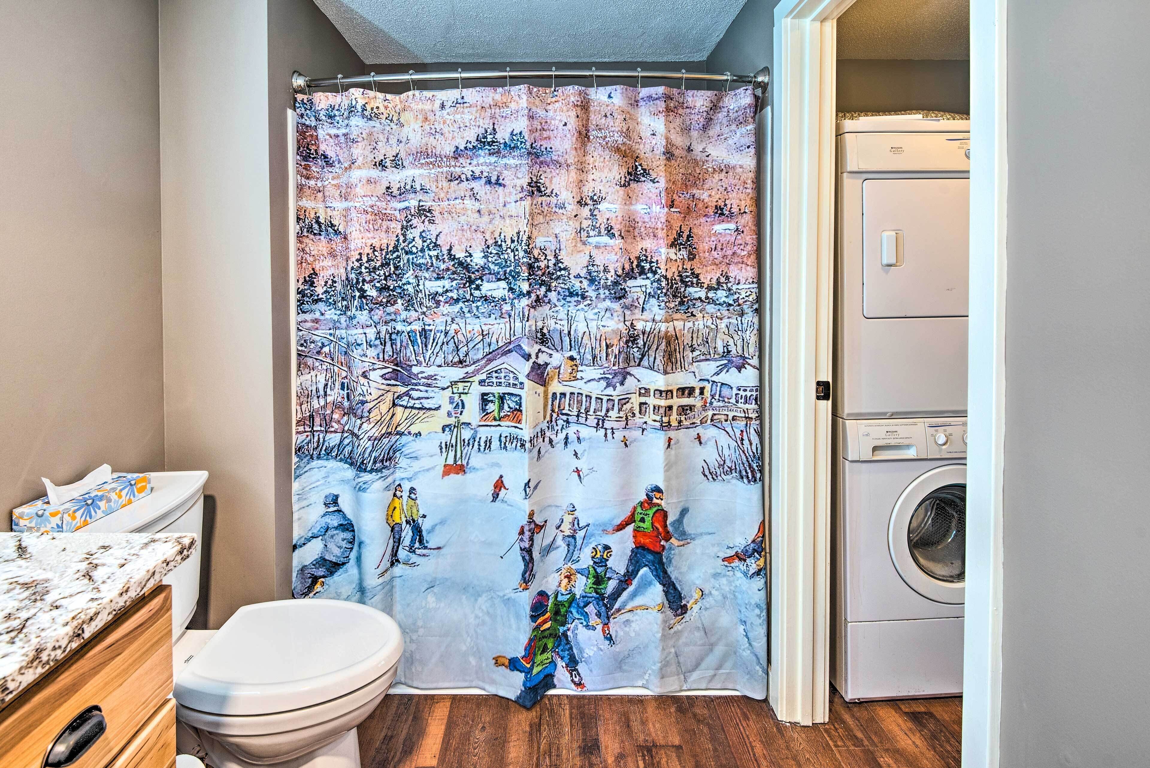 A bathroom with a winter-themed shower curtain, a toilet, a wooden cabinet, and a washing machine.