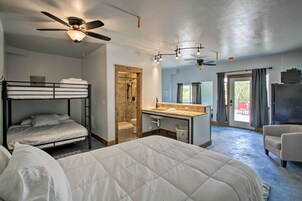 Habitación de hotel con literas, un escritorio, una silla, ventilador de techo y zona de ducha.
