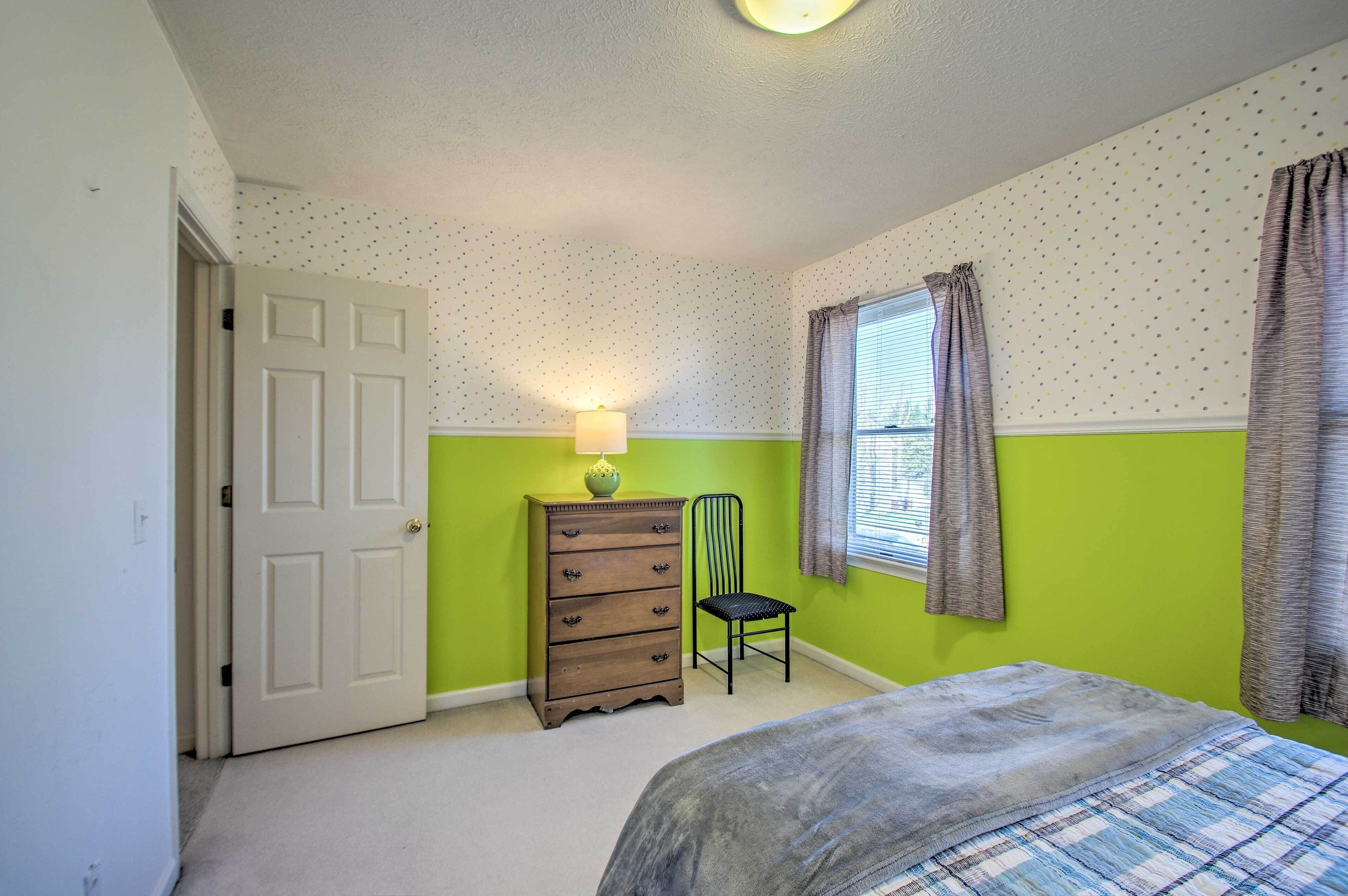 A bedroom with a bed, a dresser, a chair, and a window with curtains.