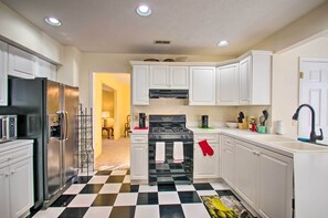 A kitchen with white cabinets, a black and white checkered floor, a stainless steel refrigerator, and a stove.