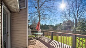 A wooden deck with a table and chairs, a red umbrella, and a view of a fenced yard and trees. - Central Harrisonburg Home w/ Fenced-in Yard! (Harrisonburg)
