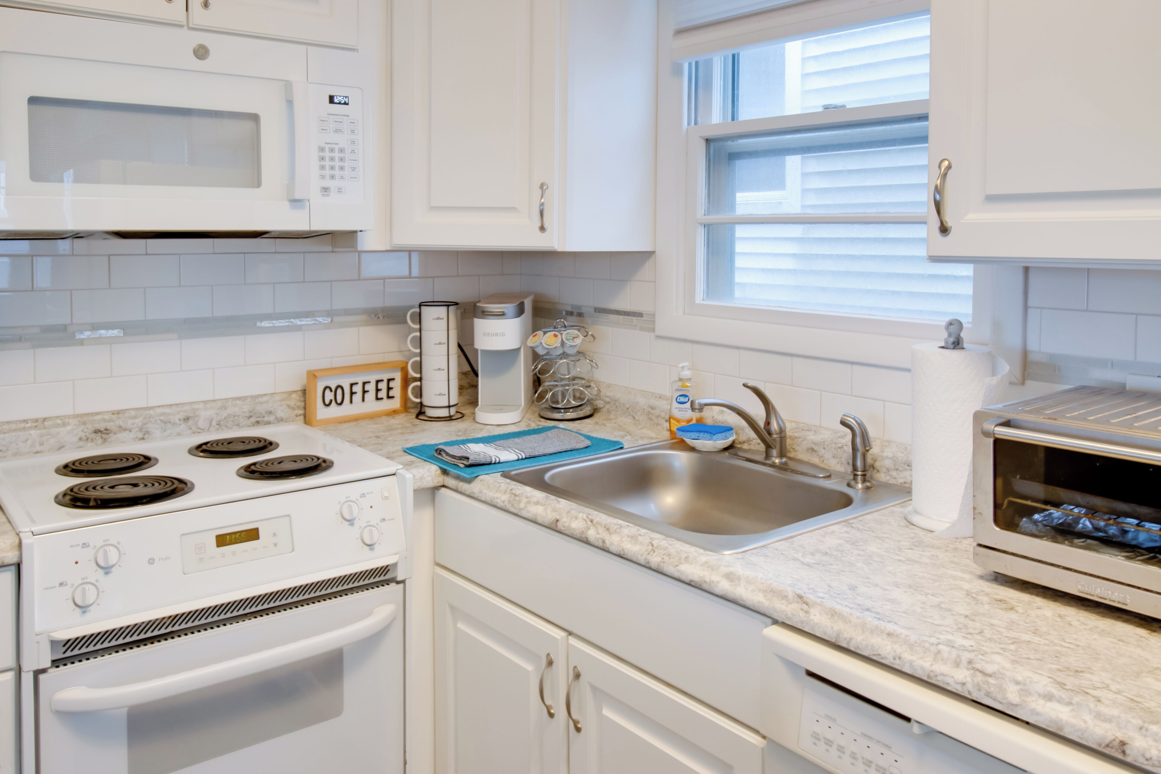 A modern kitchen with white cabinets, a built-in microwave, a stove, a sink, and a toaster oven.