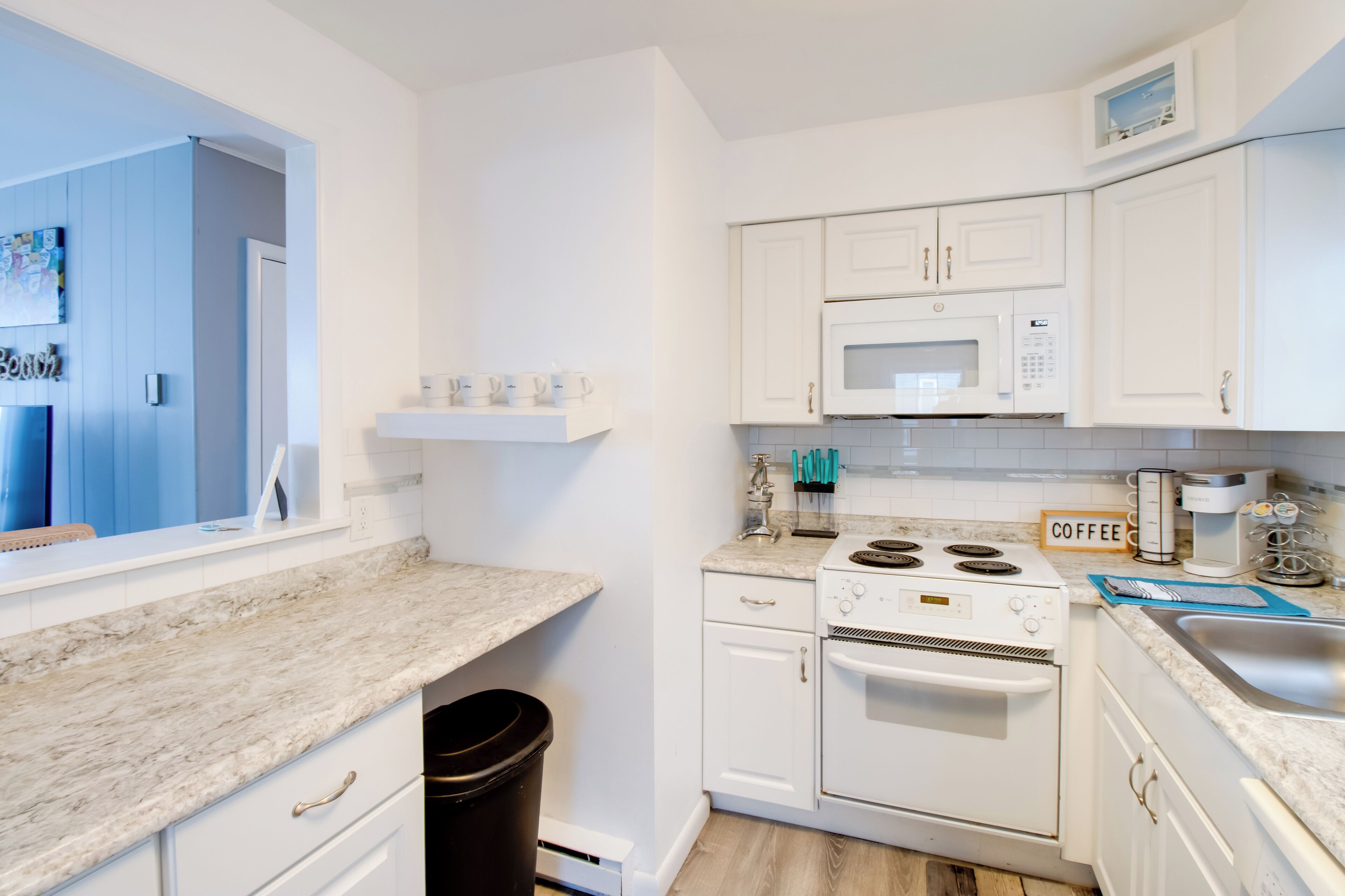 A modern kitchen with white cabinets, a built-in microwave, a stove, and a coffee station.