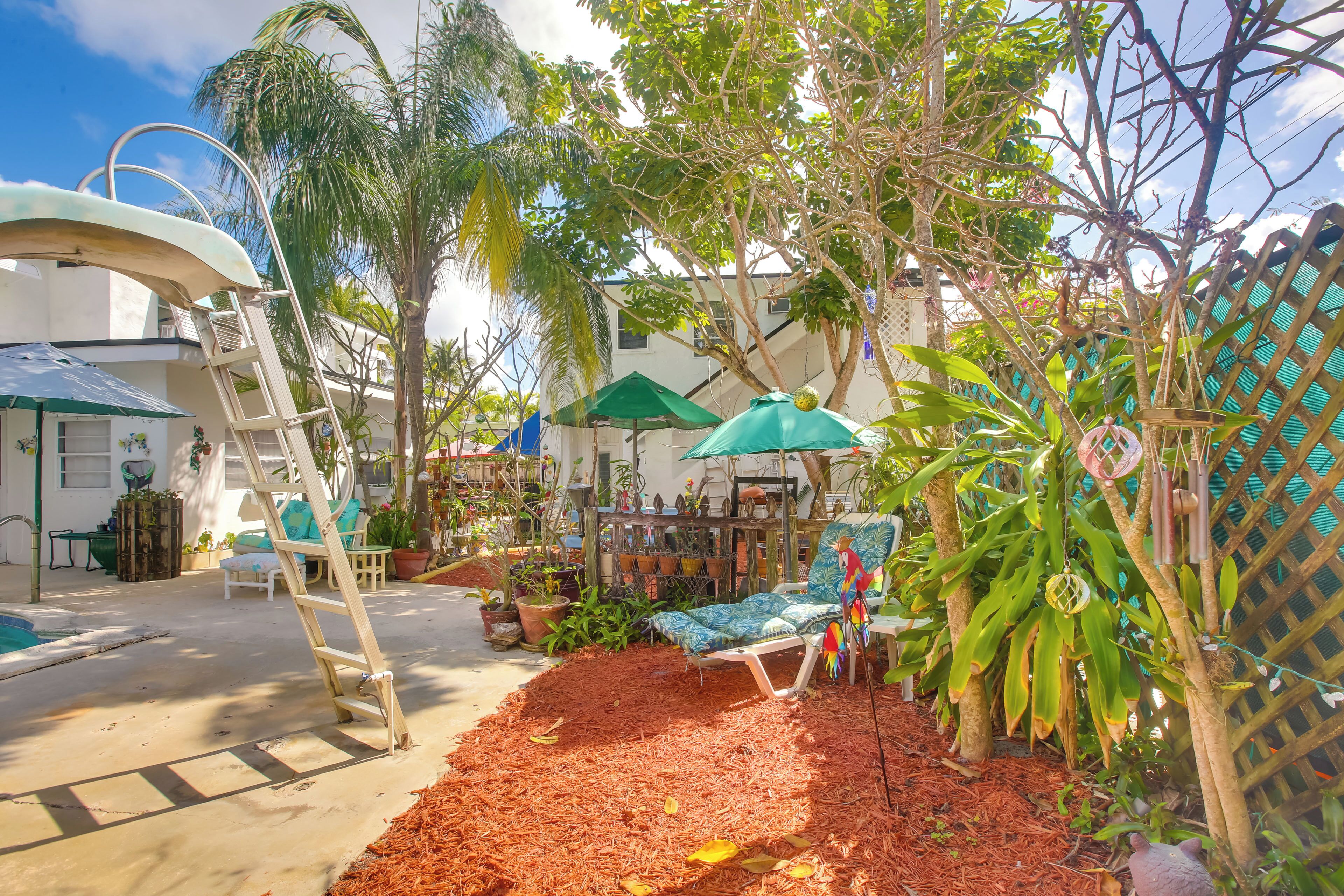 A covered outdoor seating area with a pool, surrounded by potted plants and a wooden fence.