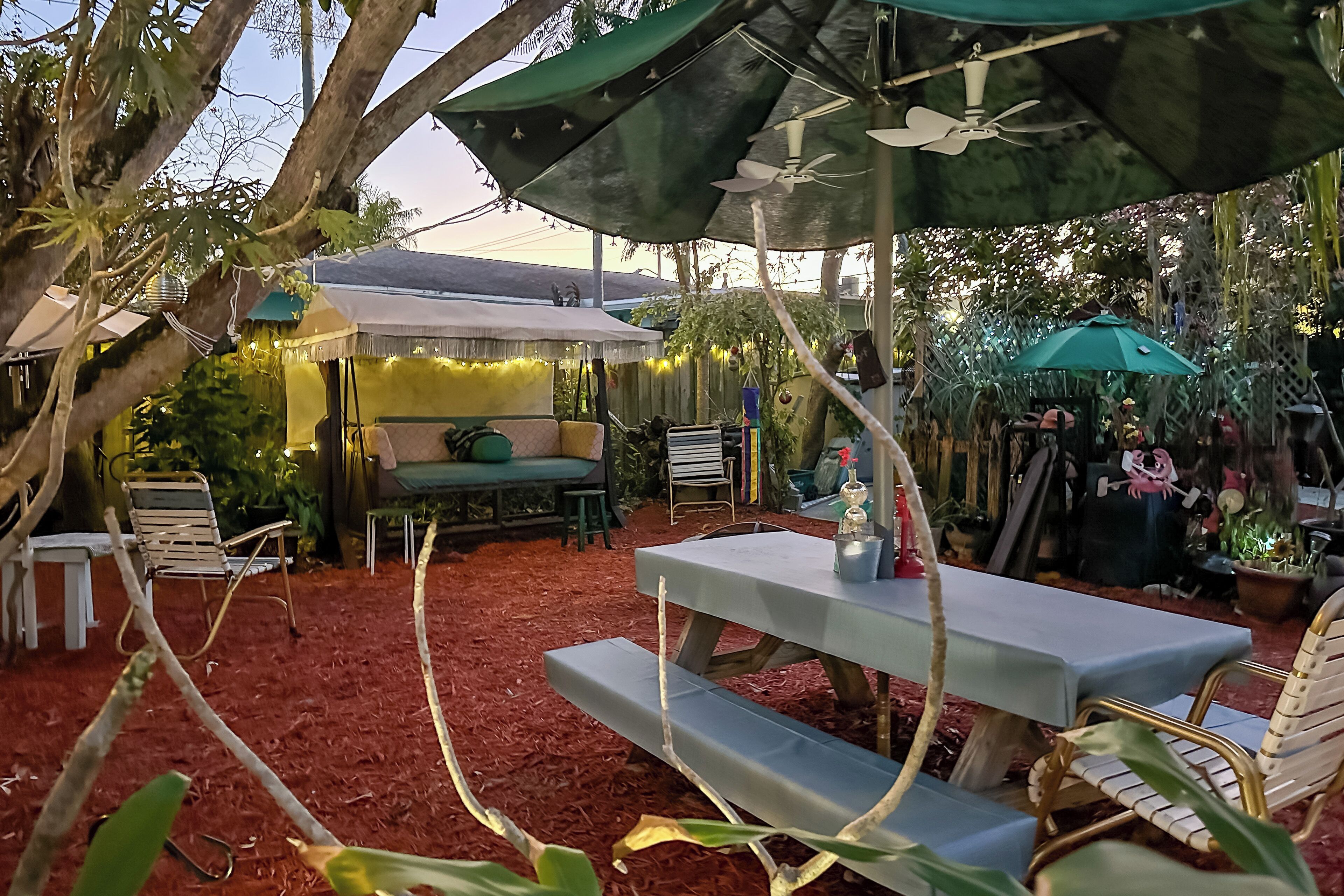 Eine Außenpatio-Terrasse mit überdachter Sitzgelegenheit, einem Picknicktisch und verschiedenen Kübelpflanzen.