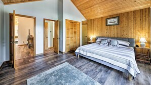 Een slaapkamer met een houten plafond, een groot bed met een gestreept laken, een nachtkastje met een lamp en een lijst met een foto aan de muur.
