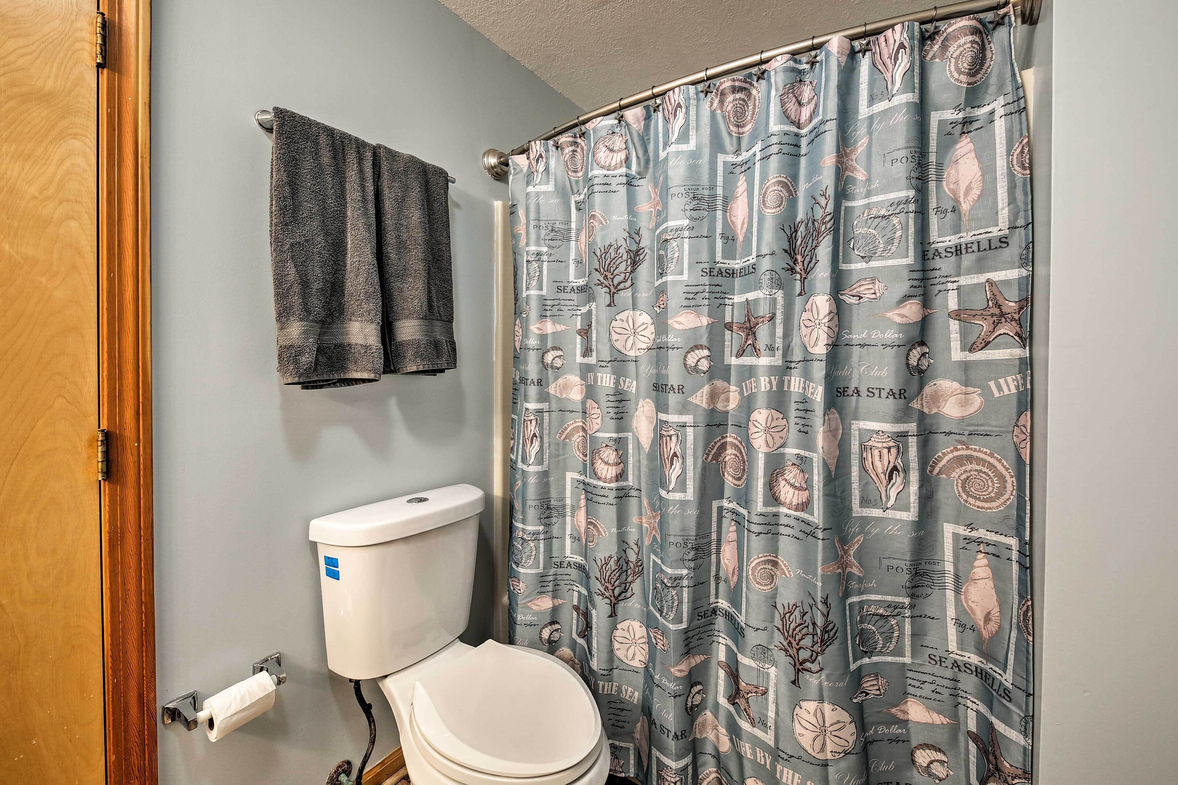 A bathroom with a toilet, a towel rack with two towels, and a shower curtain with a seashell pattern.