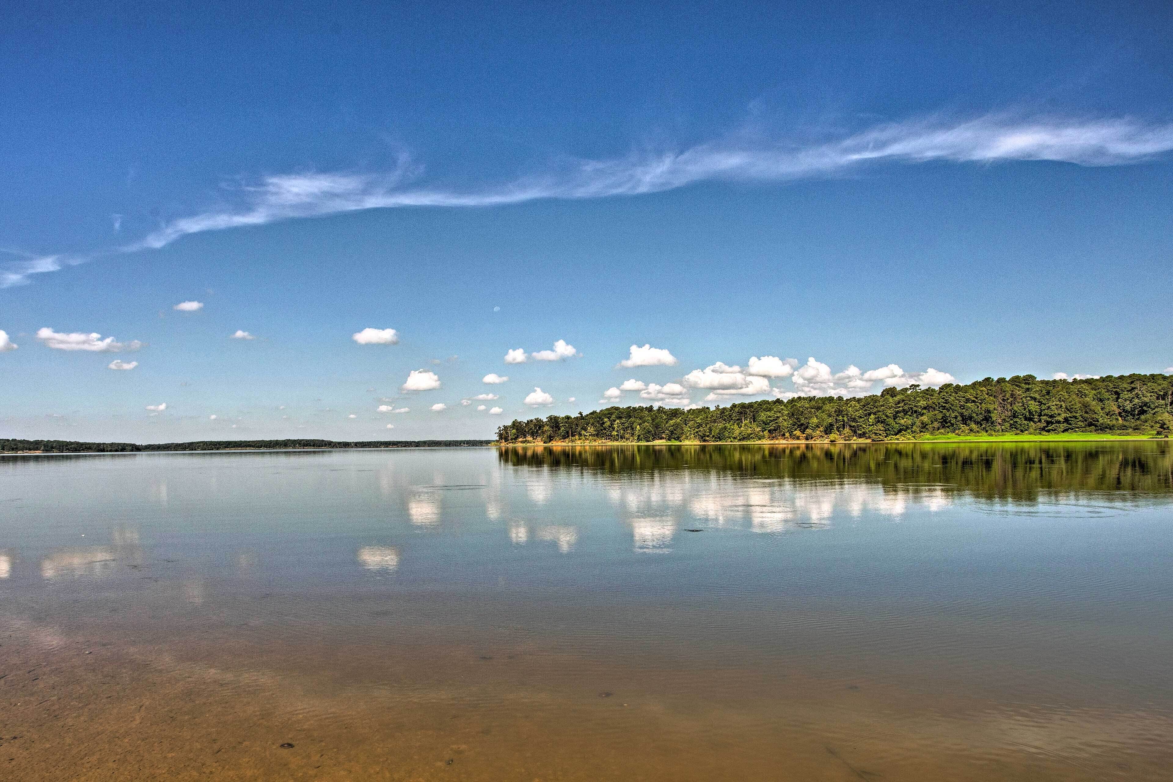 Un lago tranquilo con cielo despejado y una colina boscosa al fondo.
