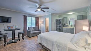 Habitación de hotel con cama, escritorio con silla, ventilador de techo, lavadora y microondas.