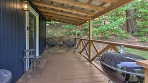 Una terraza de madera con zona cubierta, una parrilla y mobiliario de exterior.