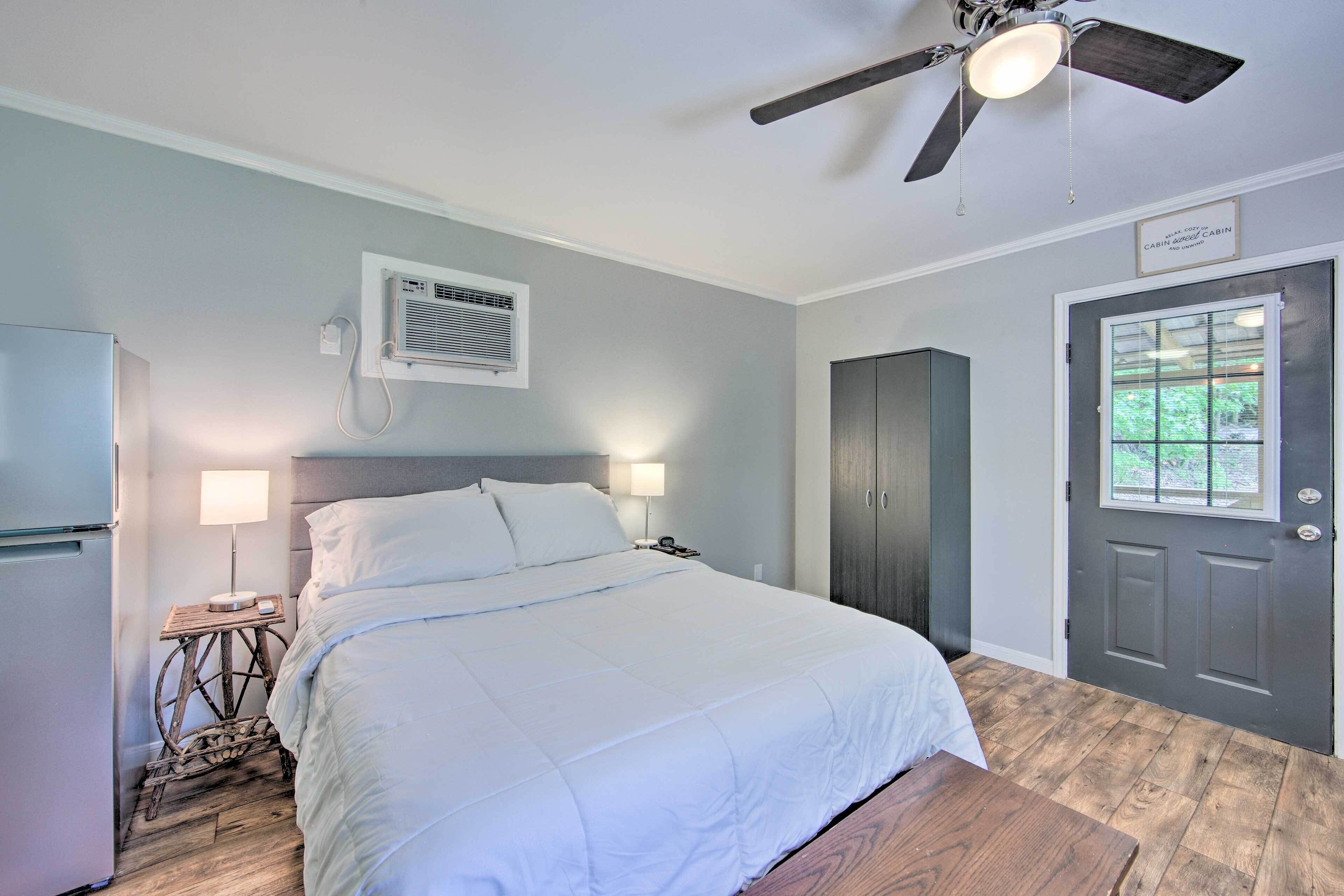 Une chambre à coucher comprenant un lit, des lampes de chevet, un ventilateur de plafond, un appareil de climatisation, une porte et une fenêtre.