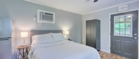 Une chambre à coucher comprenant un lit, des lampes de chevet, un ventilateur de plafond, un appareil de climatisation, une porte et une fenêtre.