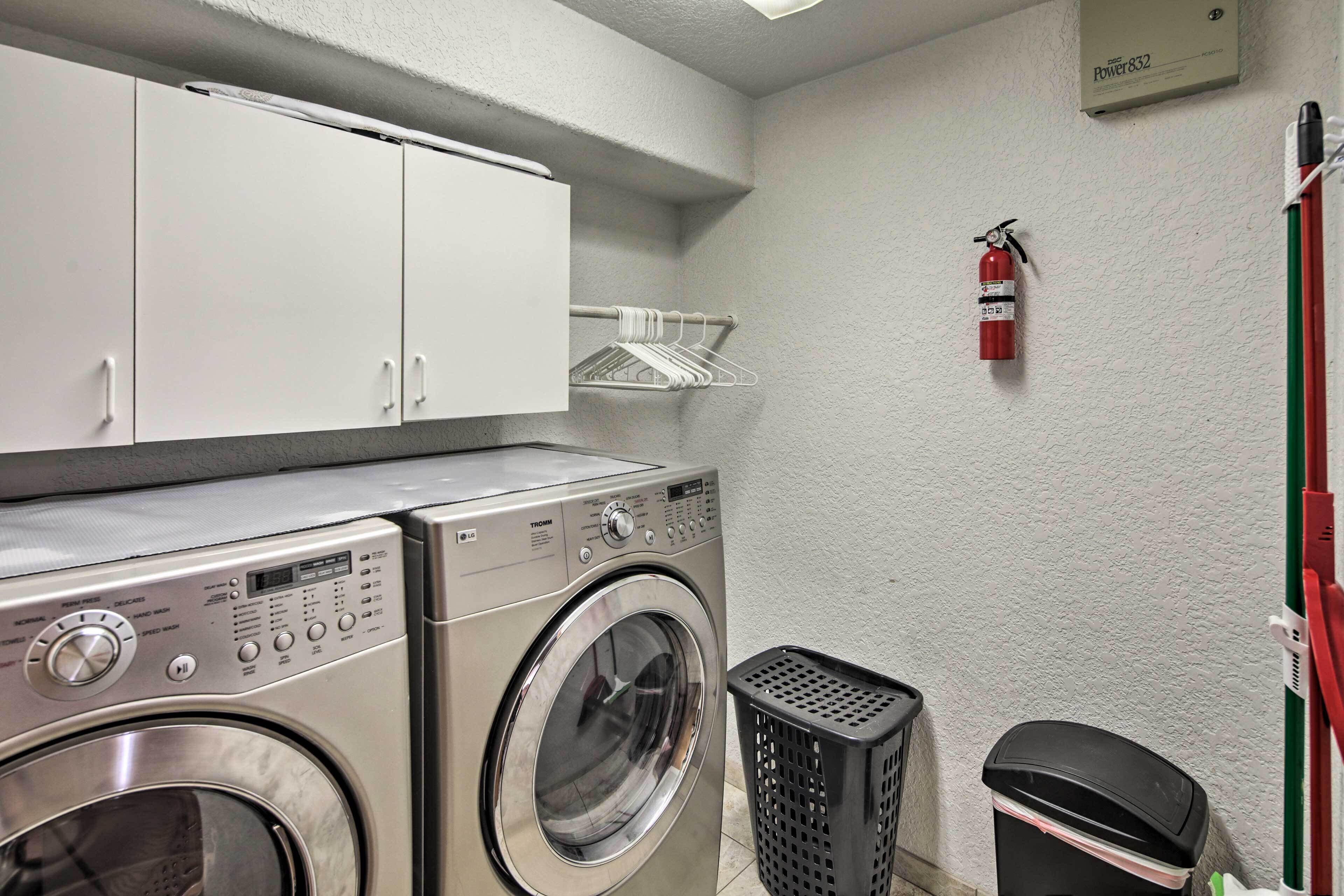 Une buanderie équipée de deux machines à laver superposées, d’un extincteur, d’un panier à linge et d’une poubelle.