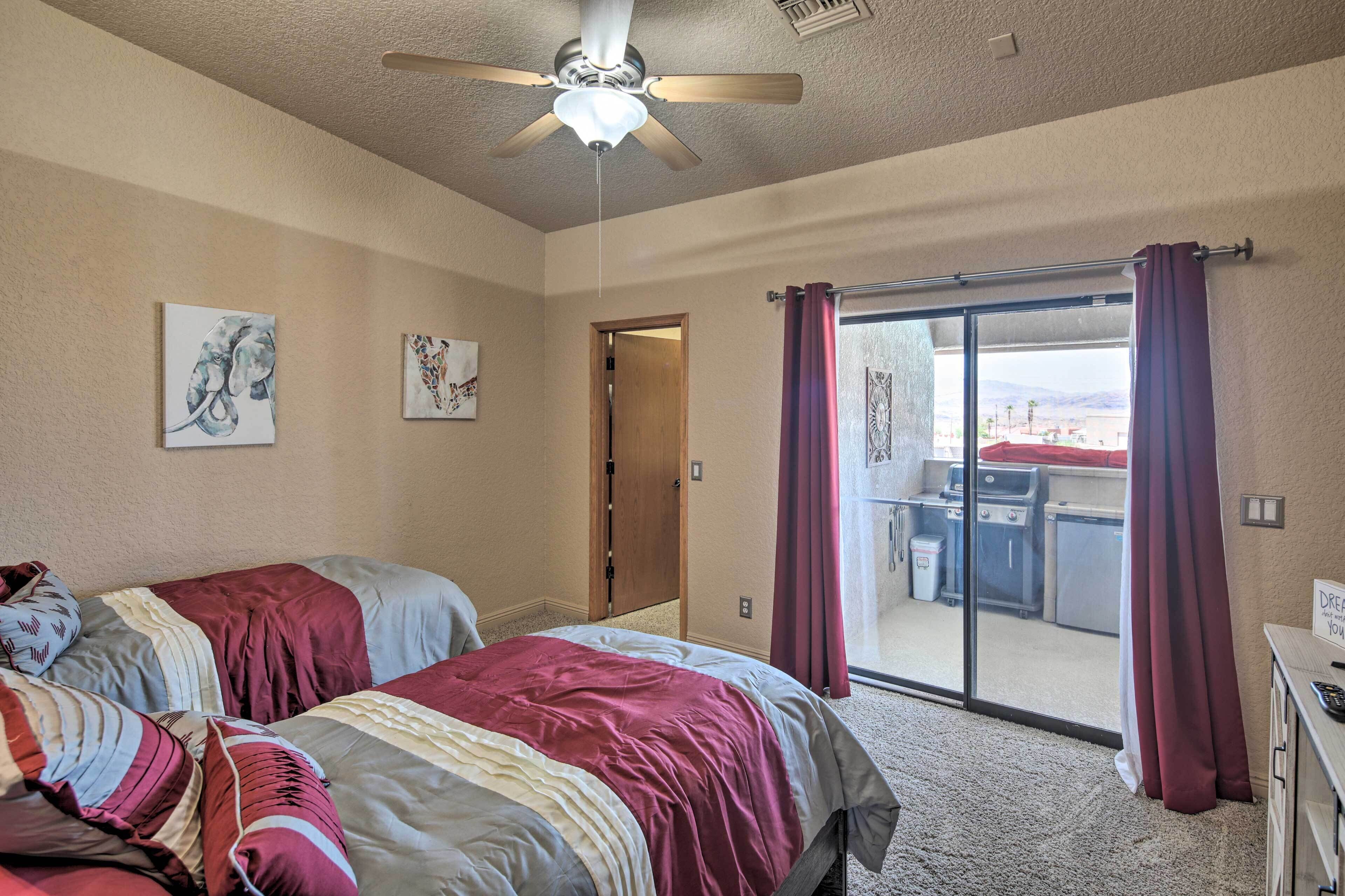 A bedroom with two beds, a ceiling fan, and a sliding glass door leading to a balcony.