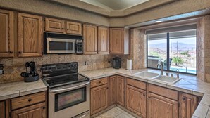 Una cocina con armarios de madera, estufa de acero inoxidable, microondas y un amplio ventanal con vistas a las montañas.