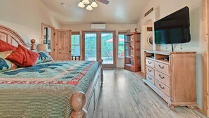 A bedroom with a large bed, wooden ceiling beams, a ceiling fan, and a television mounted on the wall. - Fire Pit, Deck & Grill: Serene Prescott Cabin! (Prescott)