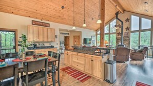 A spacious kitchen with wooden cabinets, a granite countertop, and a dining area with a table and chairs. - Fire Pit, Deck & Grill: Serene Prescott Cabin! (Prescott)