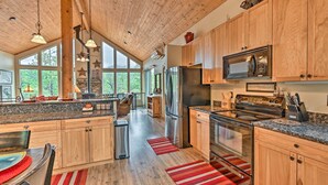 A spacious kitchen with wooden cabinets, stainless steel appliances, and large windows offering a view of the outdoors. - Fire Pit, Deck & Grill: Serene Prescott Cabin! (Prescott)