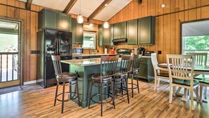 Een keuken met houten wanden, een centraal eiland met krukken, en een eethoek met stoelen.