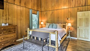 Een slaapkamer met houten lambrisering, een bed, bedlampen, een dressoir en een bankje.