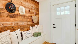 A room with a wooden wall, a white door, and a bench with pillows and bags.